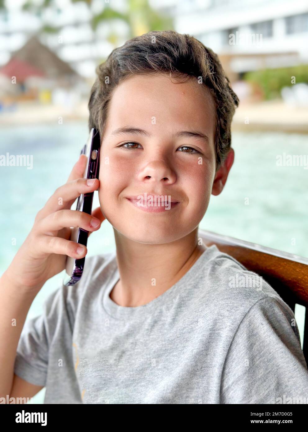 Close up portrait Happy teenage guy talking on mobile phone sitting on the beach Stock Photo