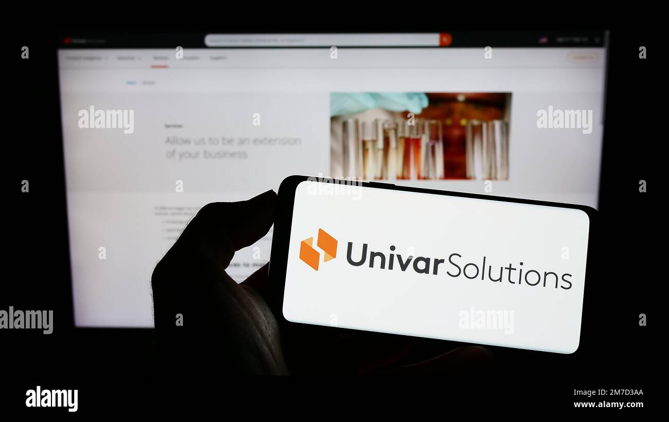 Person holding cellphone with logo of US distribution company Univar Solutions Inc. on screen in front of webpage. Focus on phone display. Stock Photo