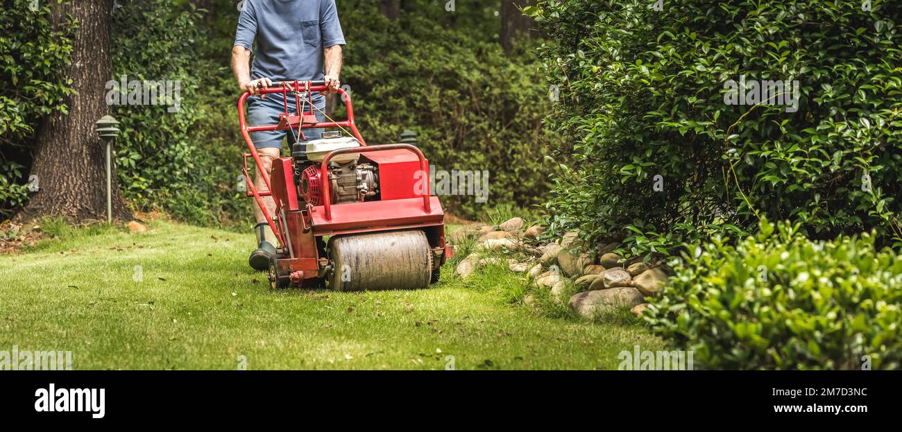 Man using gas powered aerating machine to aerate residential grass yard