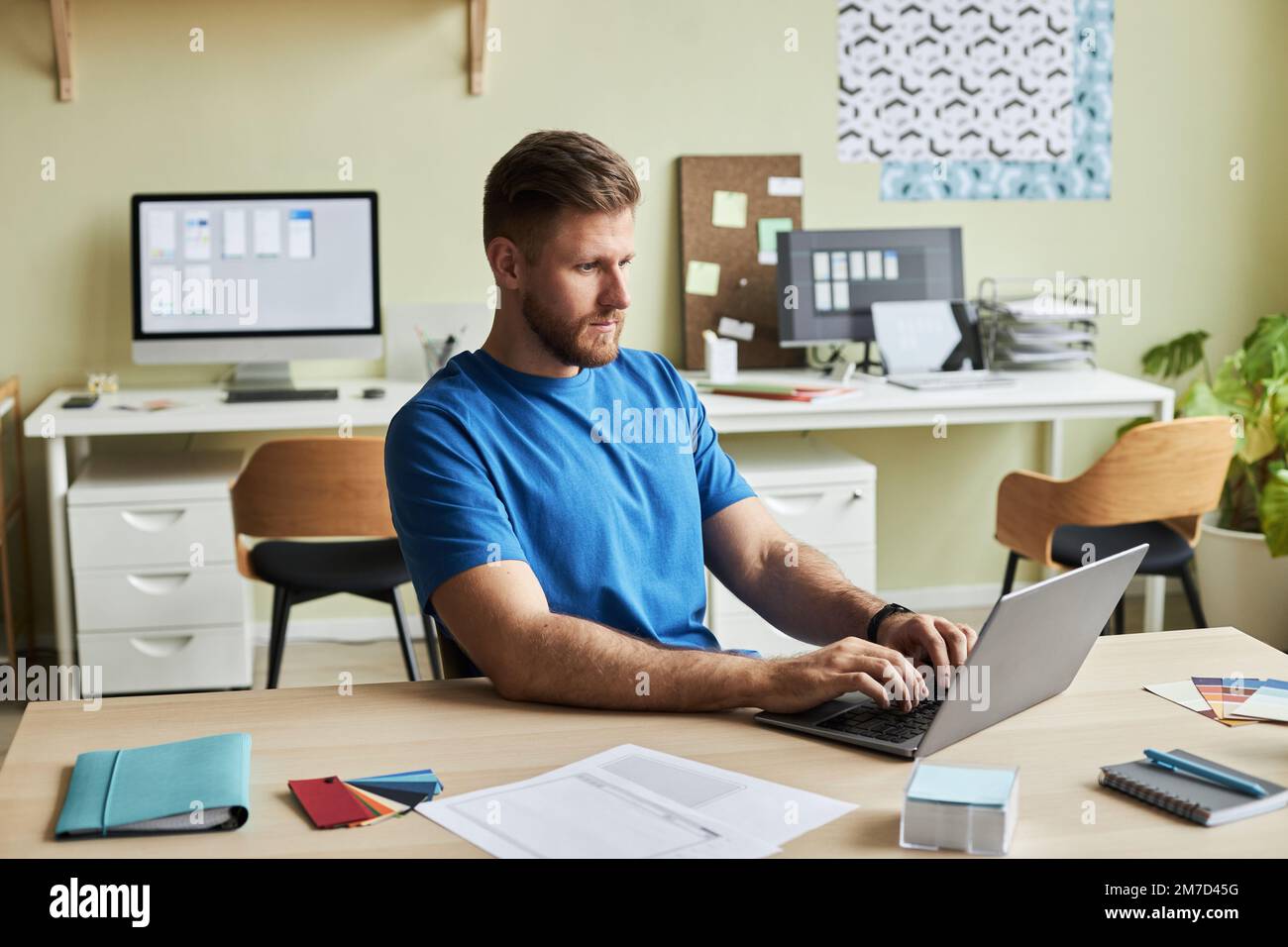 Portrait of bearded young man using laptop while working at desk in cozy office setting, copy space Stock Photo