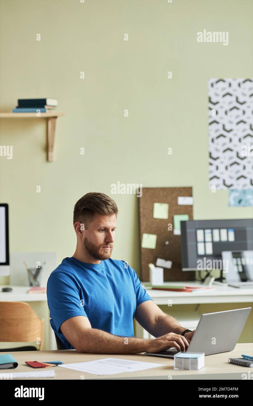 Vertical portrait of bearded young man using laptop while working at desk in minimal office setting Stock Photo