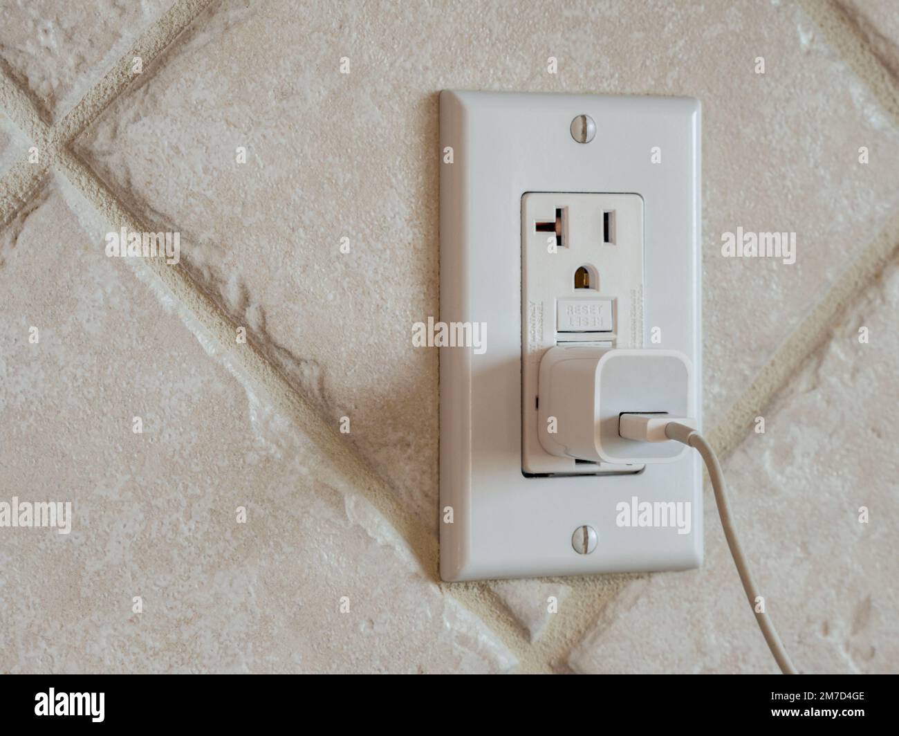 USB cell phone power adapter brick and cord in GFCI wall plug. Electrical cord and charger plug