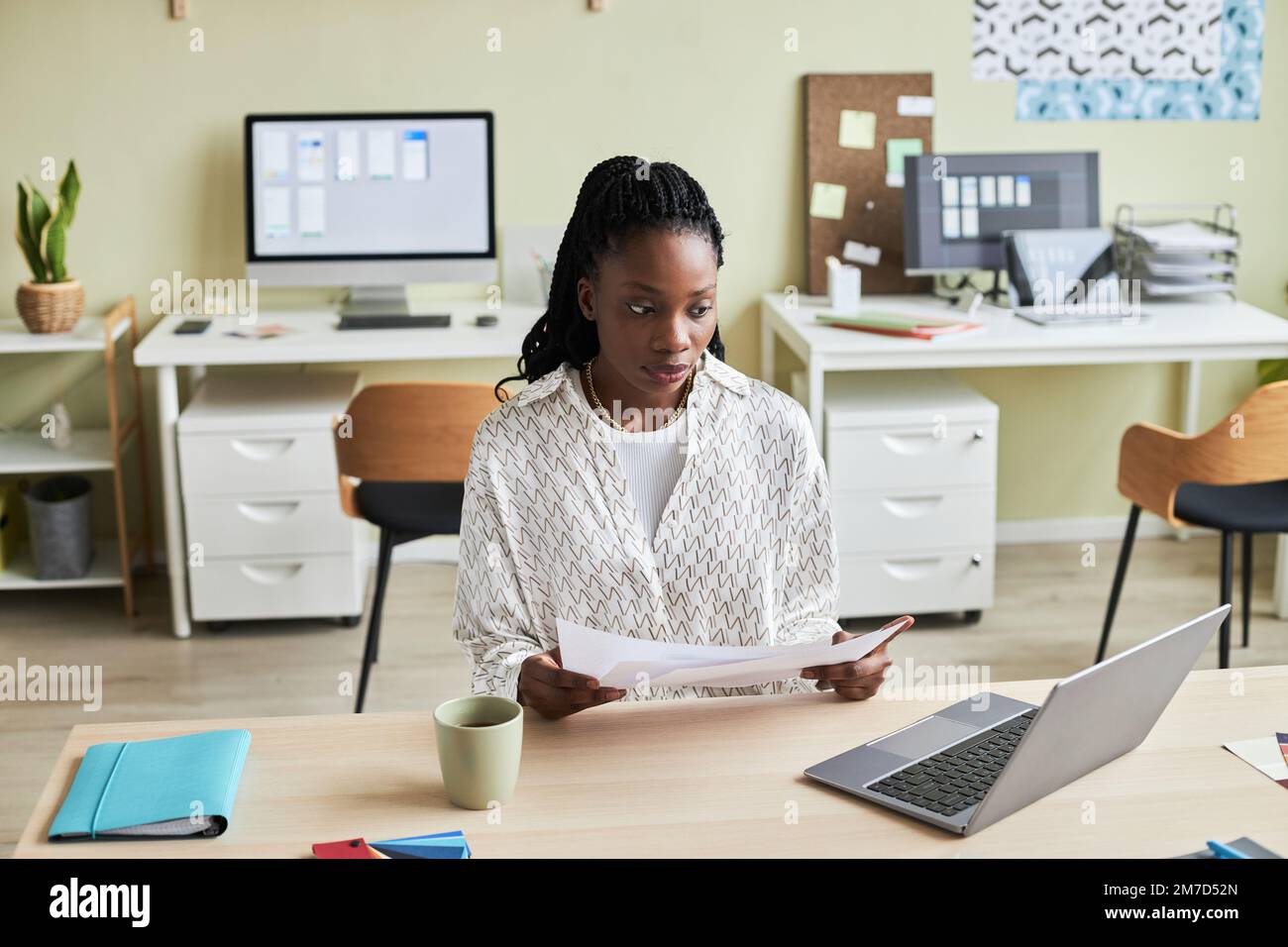 Portrait of black young woman using laptop while working at desk in cozy office setting, copy space Stock Photo