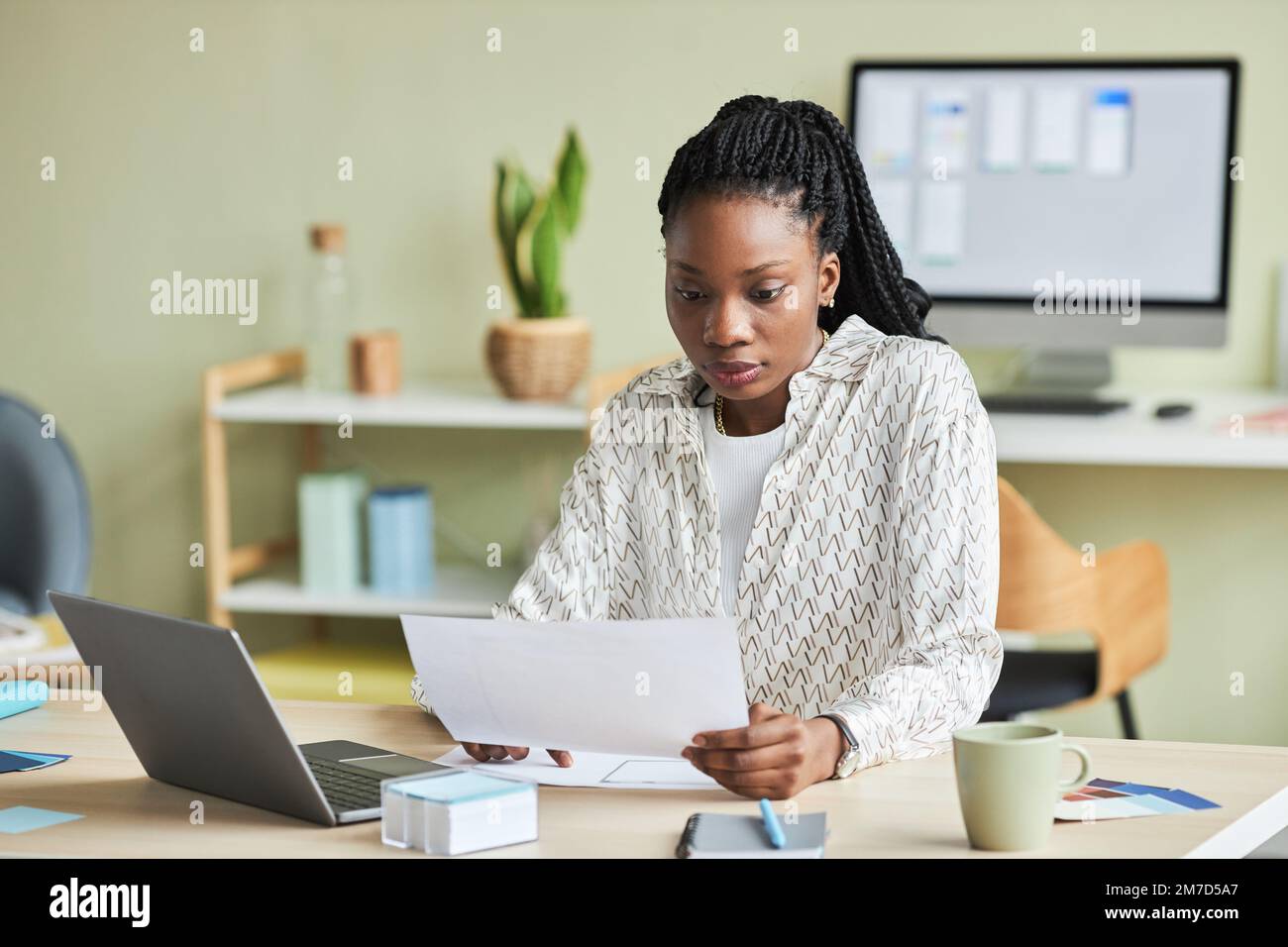 Minimal portrait of black young woman using laptop while working at desk in office setting, copy space Stock Photo