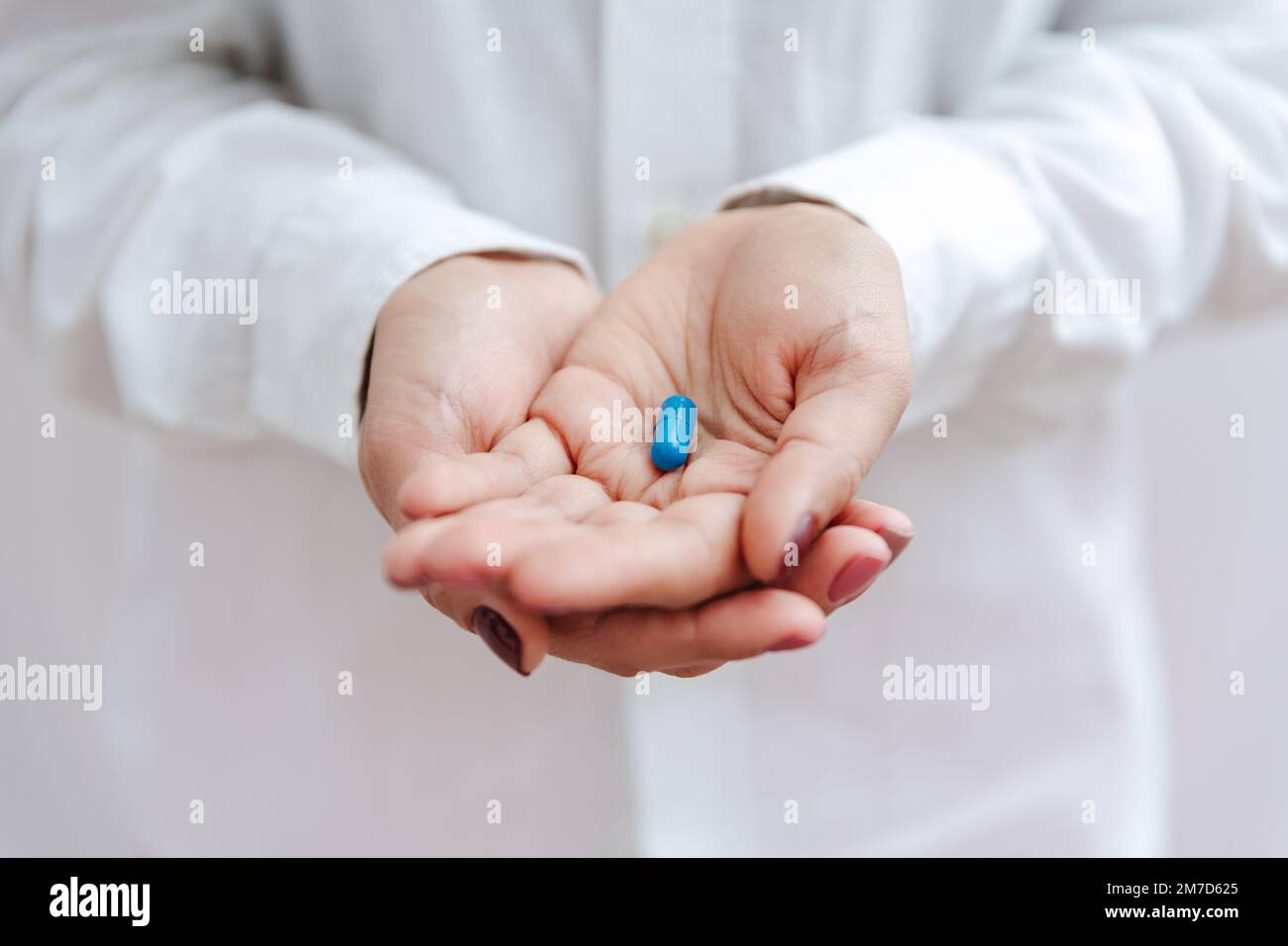 Women's hand with blue pill, vitamin, capsule. Medical insurance, medical treatment concept. Disease, sick treatment, cold season concept. Close-up vi Stock Photo