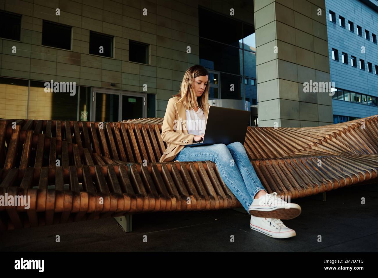 Woman sitting on bench outdoors and using laptop. Concept of remote ...