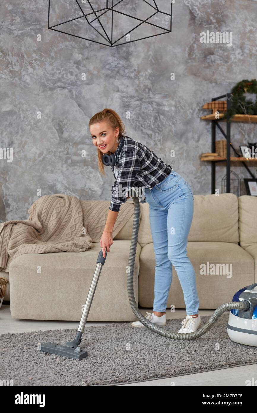 Young smiling woman vacuum cleaning the carpet in the living room ...