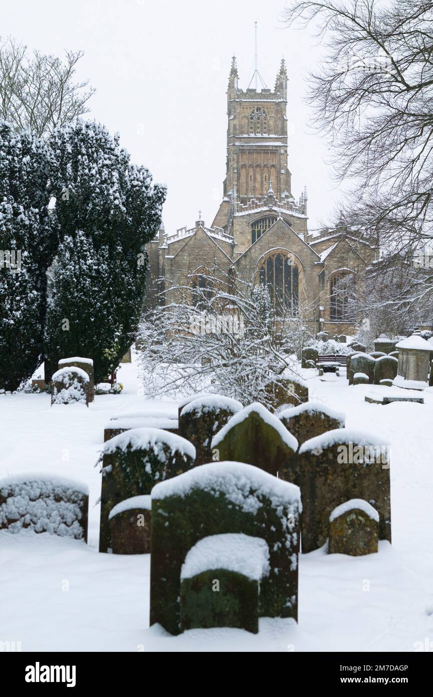 The grounds of St John the Baptist church in Cirencester, UK with graveyard in the deep snow of winter. Hidden amongst the snow stand the gravestones ion this peaceful quite scene typical of traditional British winter. Stock Photo