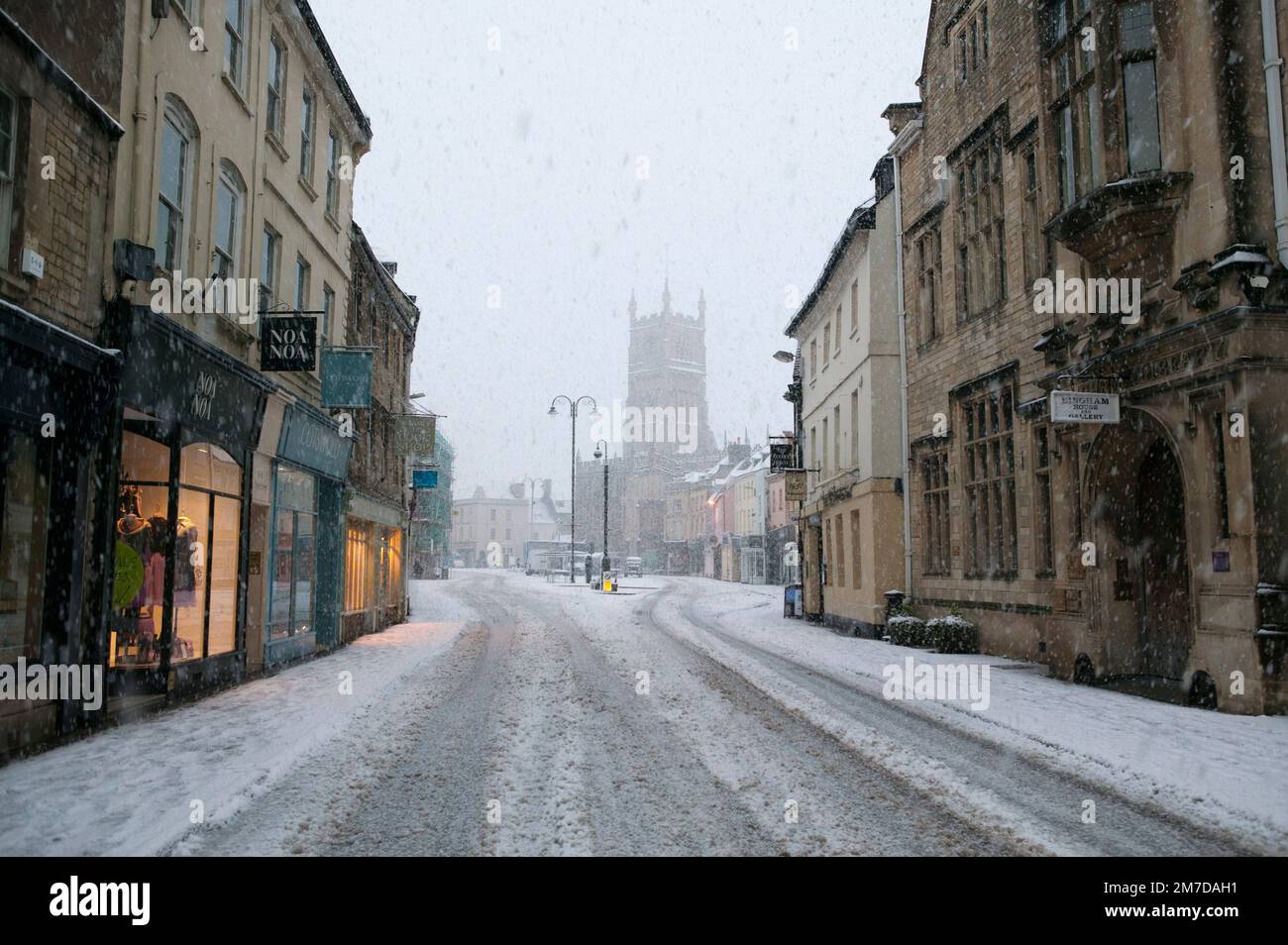 The MArket square of Cirencester in the heart of the Cotswolds, Uk covered in a layer of snow in the depths of winter. Clearly showing the tower adn church of St john the Baptist all the buildings are coverd in this unusually heavy downfall of snow. Stock Photo