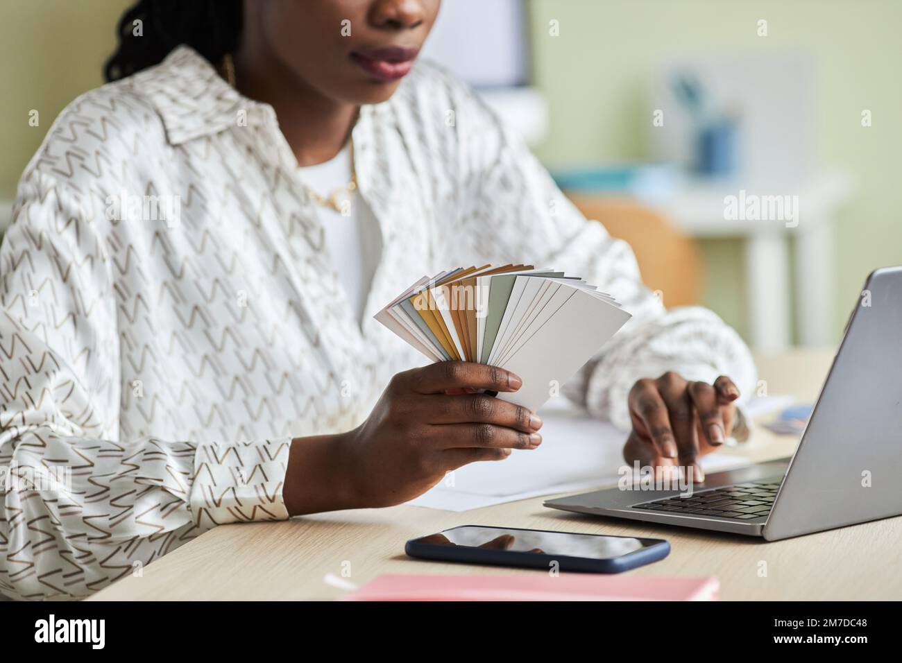 Close up of black young woman using laptop while working in office and holding color swatches, copy space Stock Photo