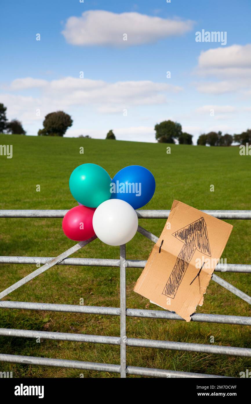 Ballons tied up with a cardboard sign set out in the country, the sign points with an arrow and the ballons mean that a party is underway and indicates the direction in which it is being held. Stock Photo
