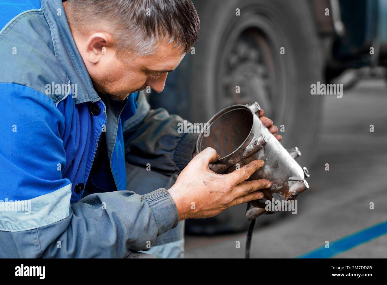 Auto mechanic repairs truck. Professional repair and diagnostics of cargo tractors and equipment. Mechanic in workshop considers spare parts.. Stock Photo