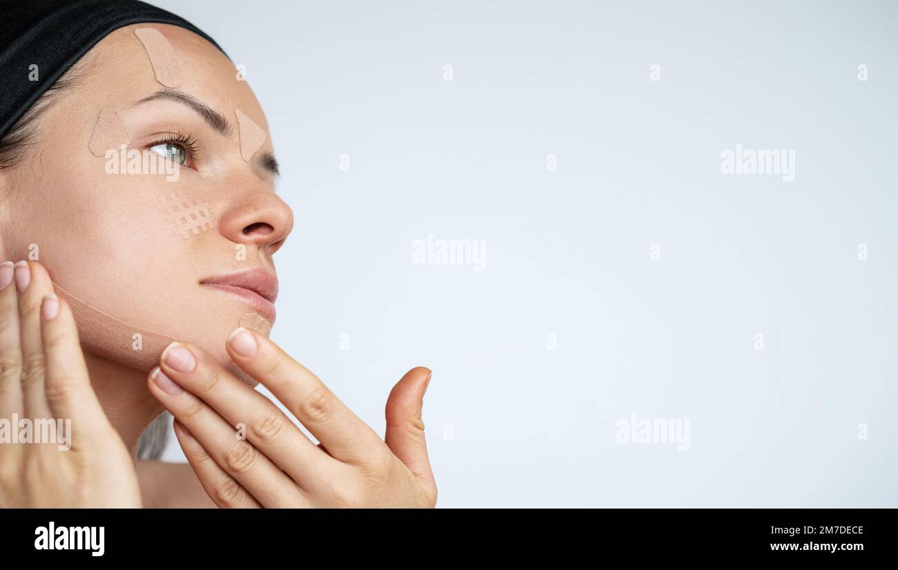 Adult woman applying facial kinesiology tape on her face facial taping
