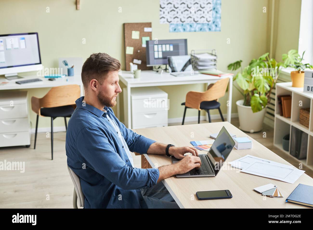 Side view portrait of bearded young man using laptop while working in cozy office, copy space Stock Photo