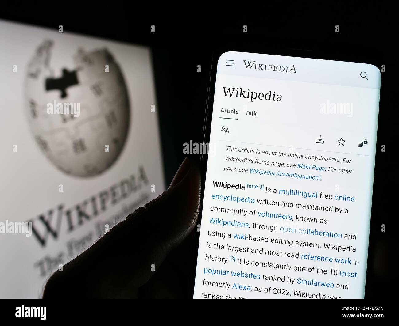 Person holding cellphone with webpage of online encyclopedia Wikipedia on screen in front of logo. Focus on center of phone display. Stock Photo
