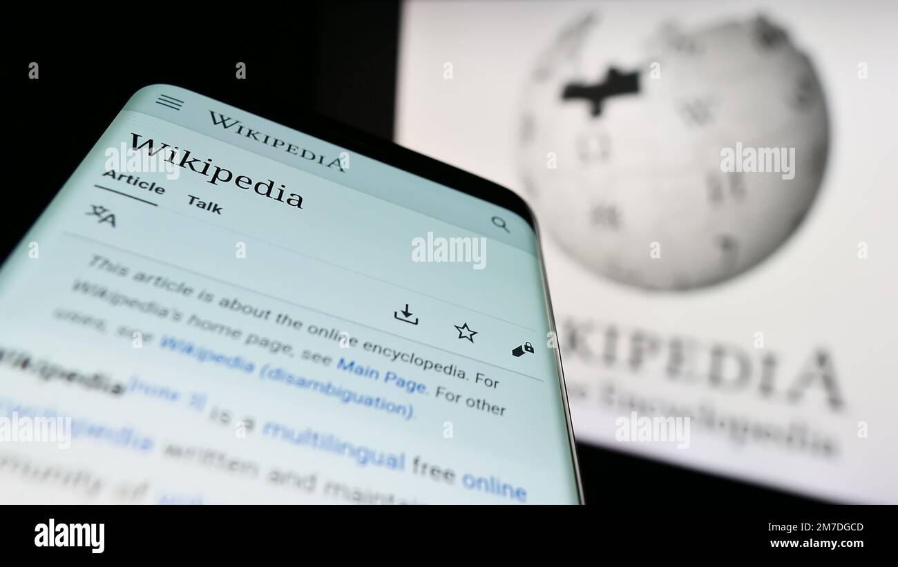 Mobile phone with webpage of online encyclopedia Wikipedia on screen in front of logo. Focus on top-left of phone display. Stock Photo