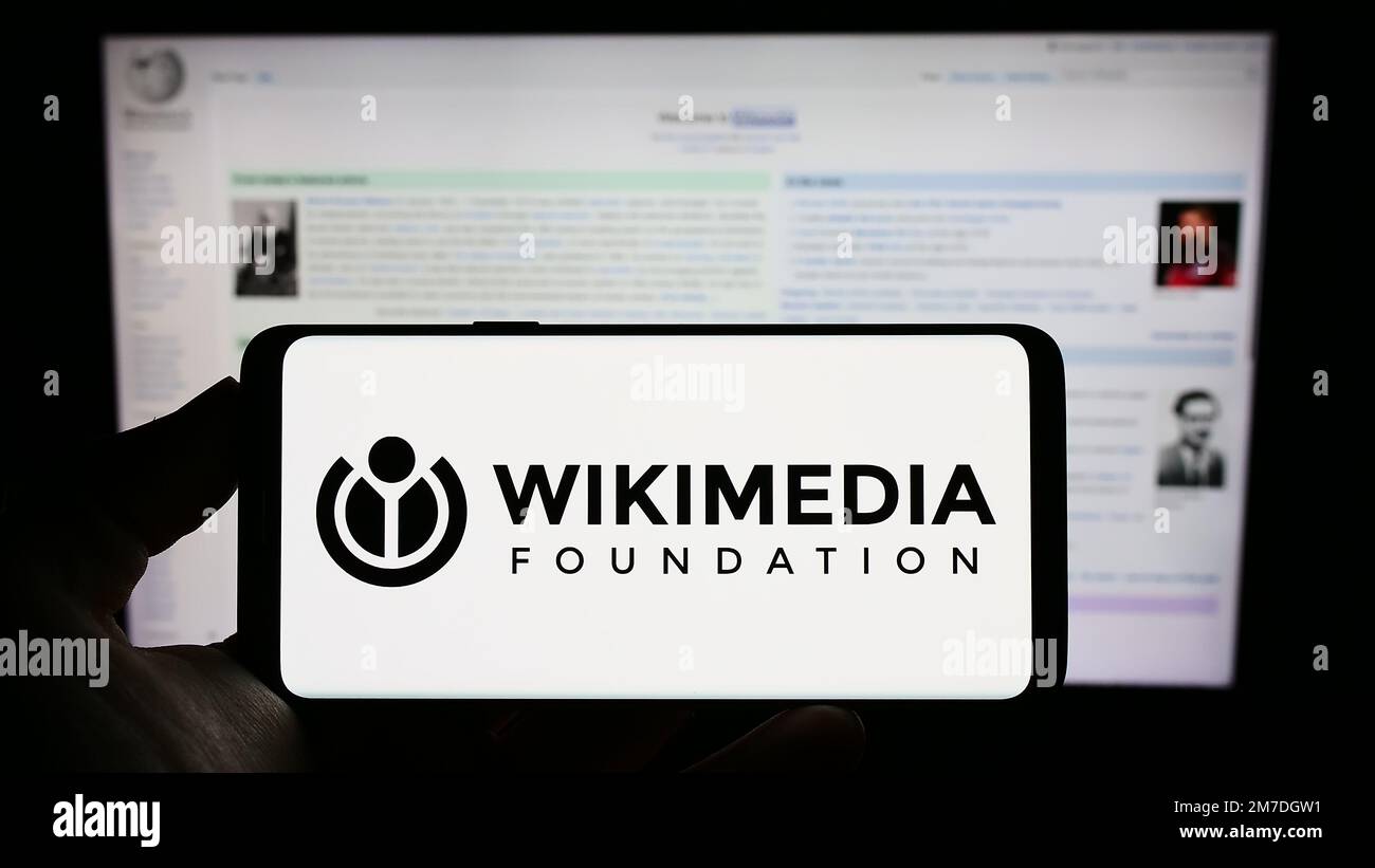 Person holding cellphone with logo of Wikimedia Foundation Inc. on screen in front of Wikipedia webpage. Focus on phone display. Stock Photo