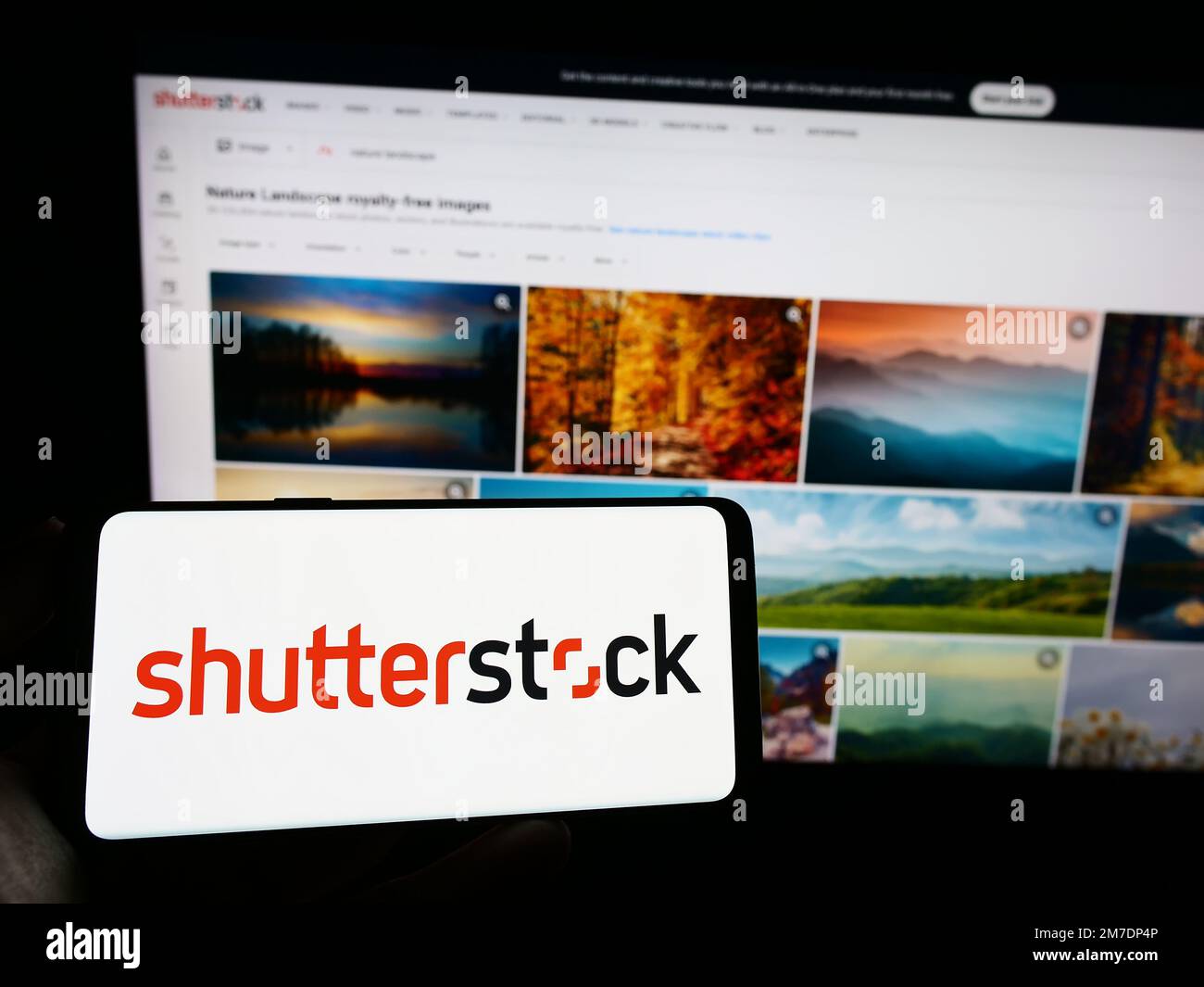 Person holding cellphone with logo of American stock photography company Shutterstock Inc. on screen in front of webpage. Focus on phone display. Stock Photo