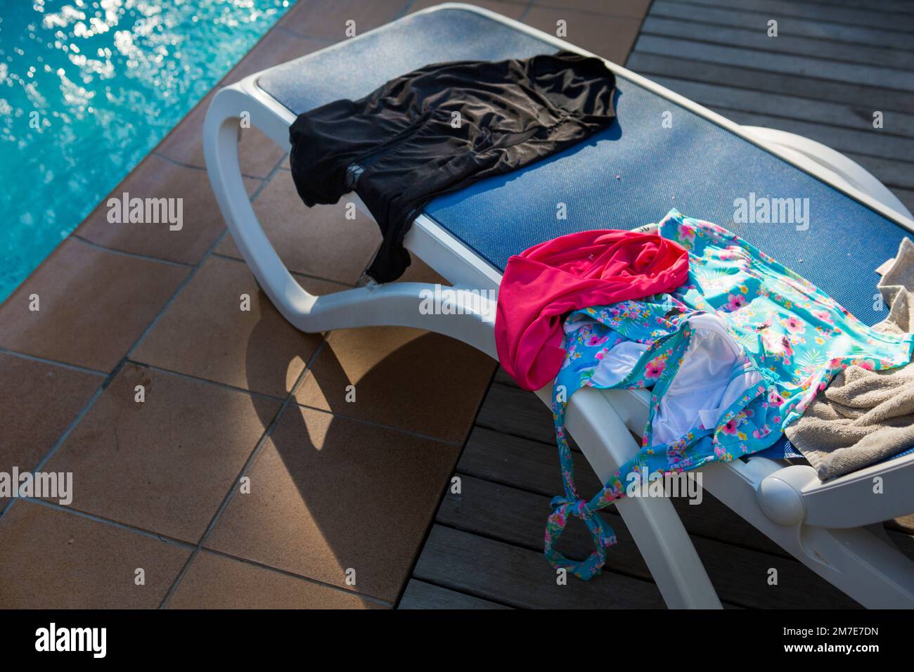A pool side lounger with swimming costume, towels and rtrunks drying in the sun. Stock Photo