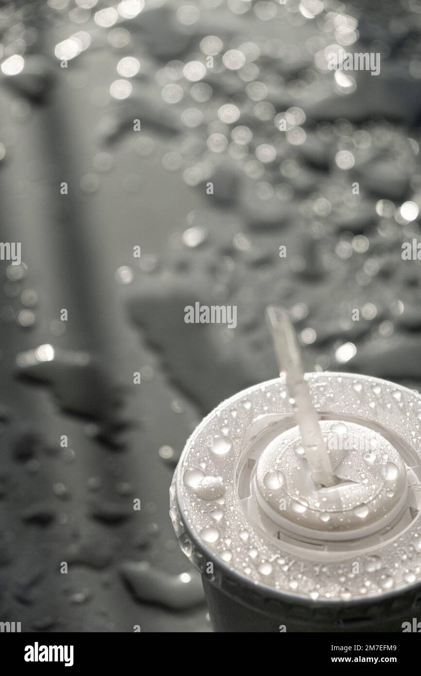 A light grey surface covered with drops and pools of water from a passsing rain shower and a plastic drinks container from a take away shop with plastic straw. Stock Photo