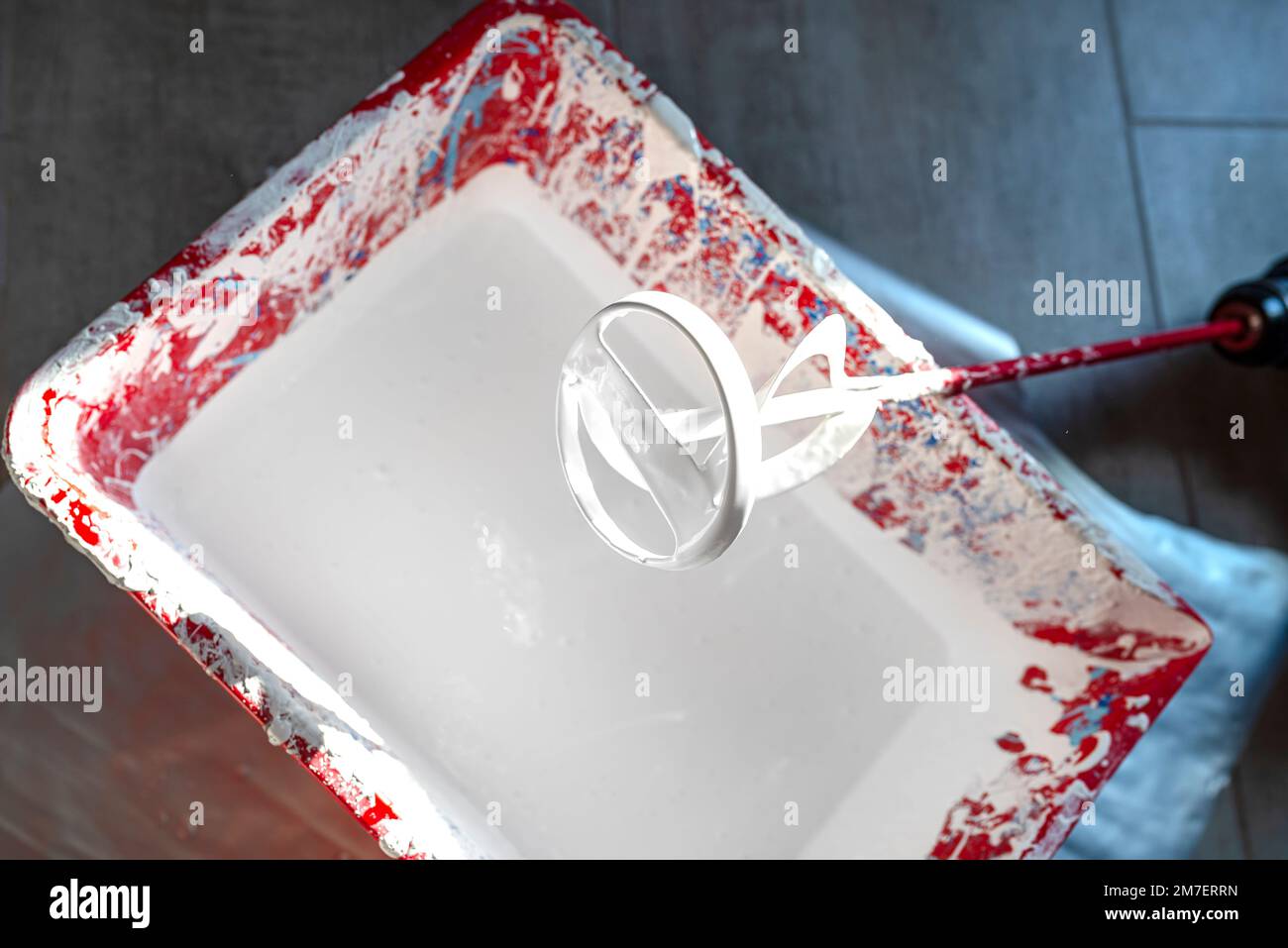 An open plastic bucket with white paint and a stirrer standing on the