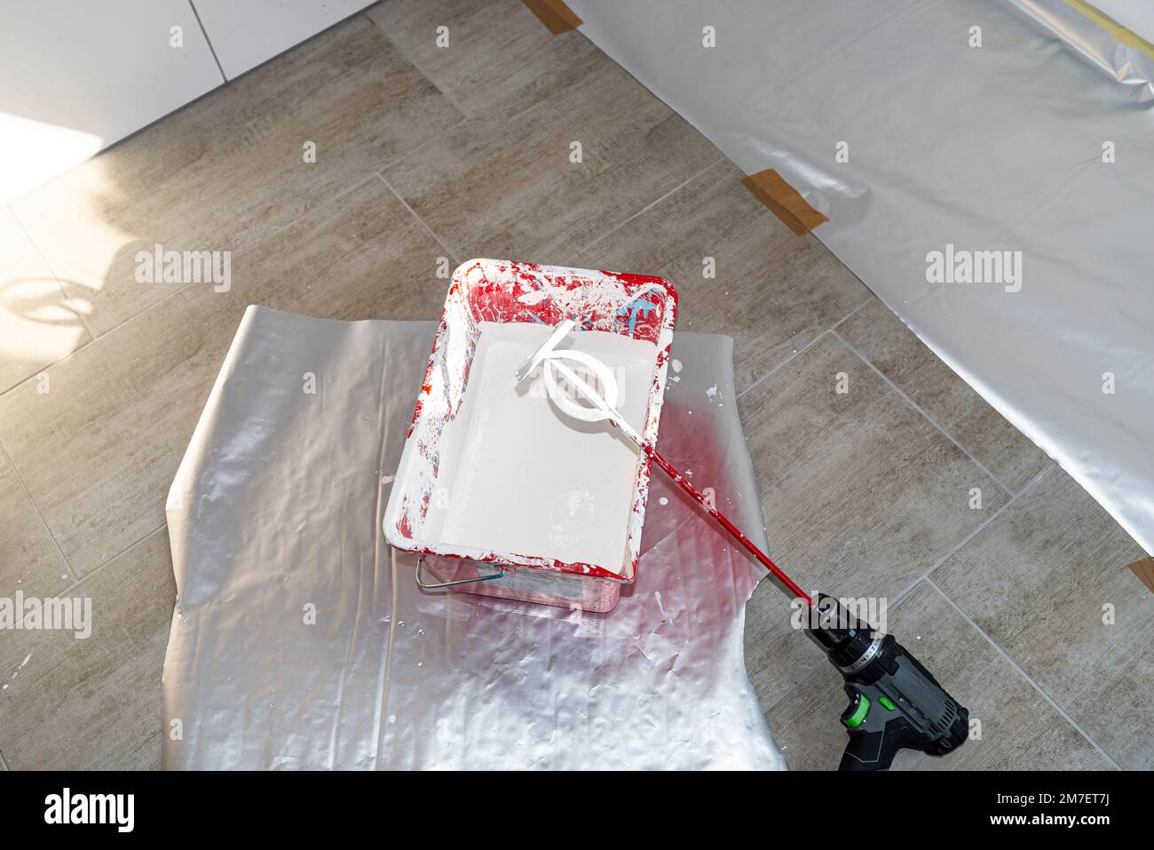 An open plastic bucket with white paint and a stirrer standing on the