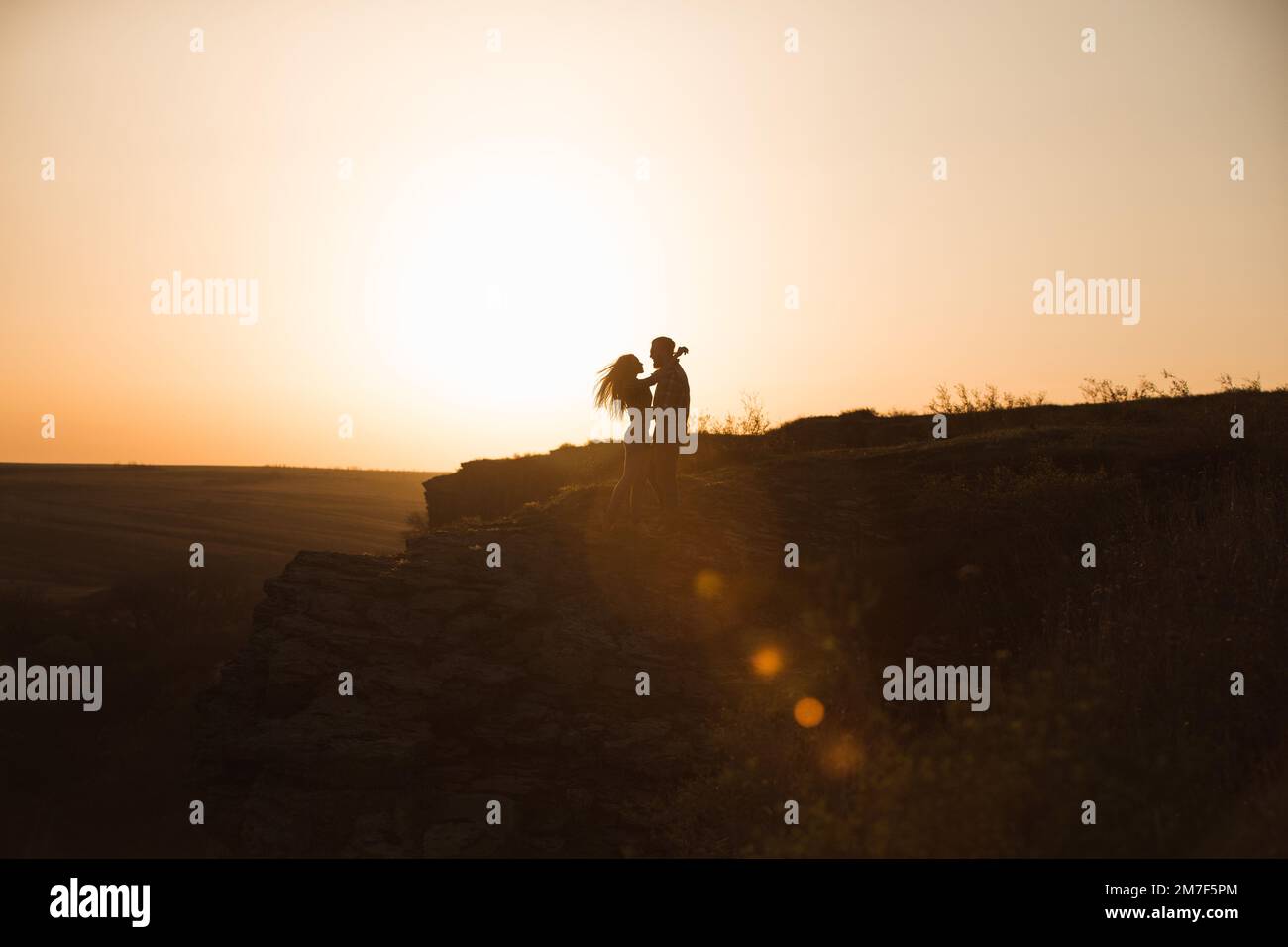 Bearded man and red-haired woman stand embracing at sunset. Stock Photo
