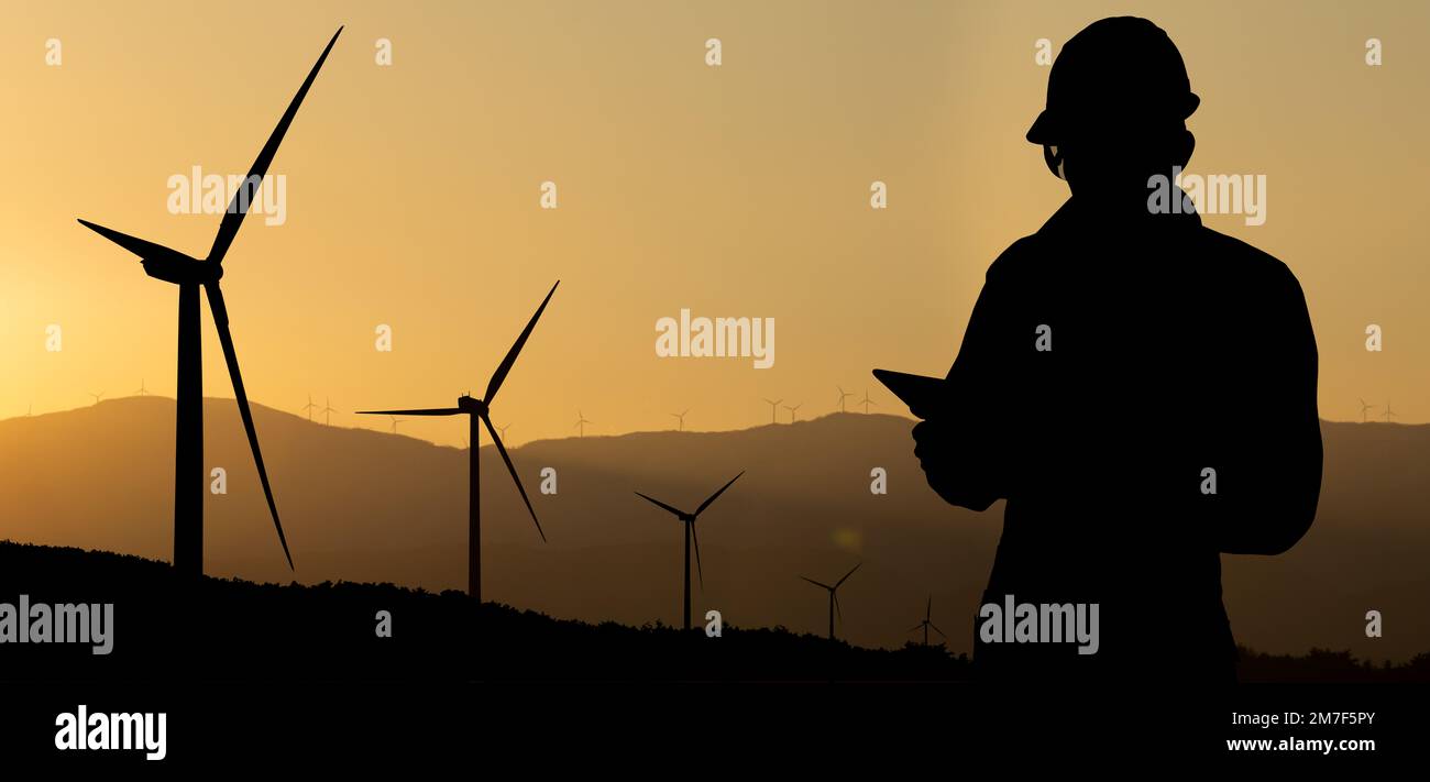 Silhouette of engineer with tablet computer and wind turbines at sunset Stock Photo