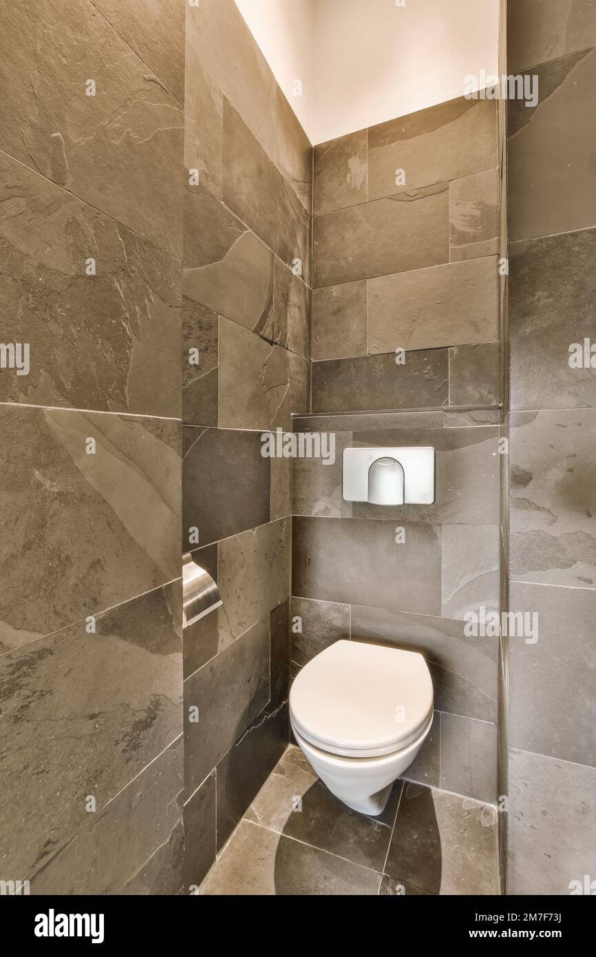 a toilet in the corner of a small bathroom with grey tiles on the walls