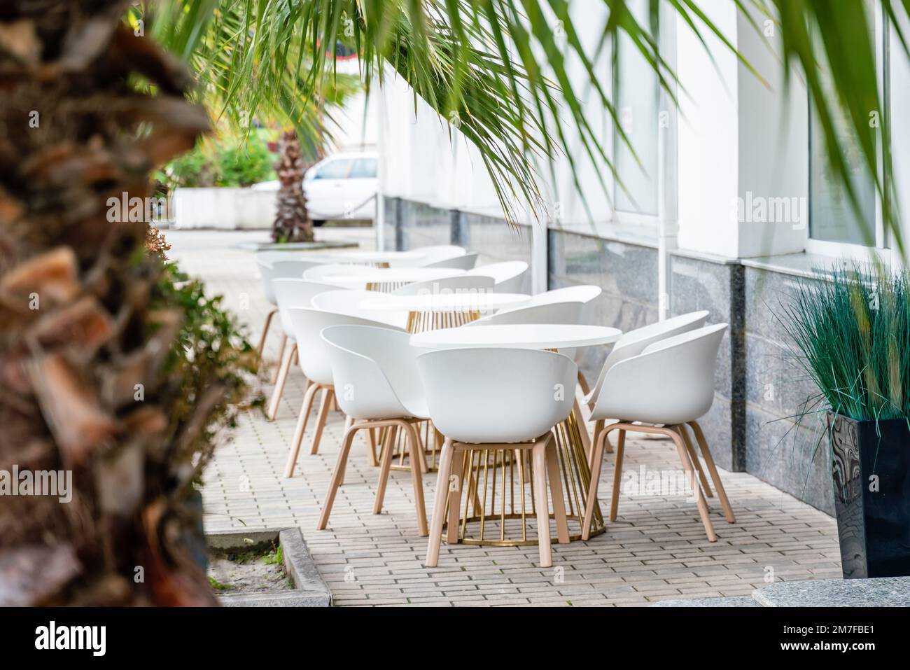 Street cafe with white chairs, green foliage around. Without people, tourism, travel. Stock Photo