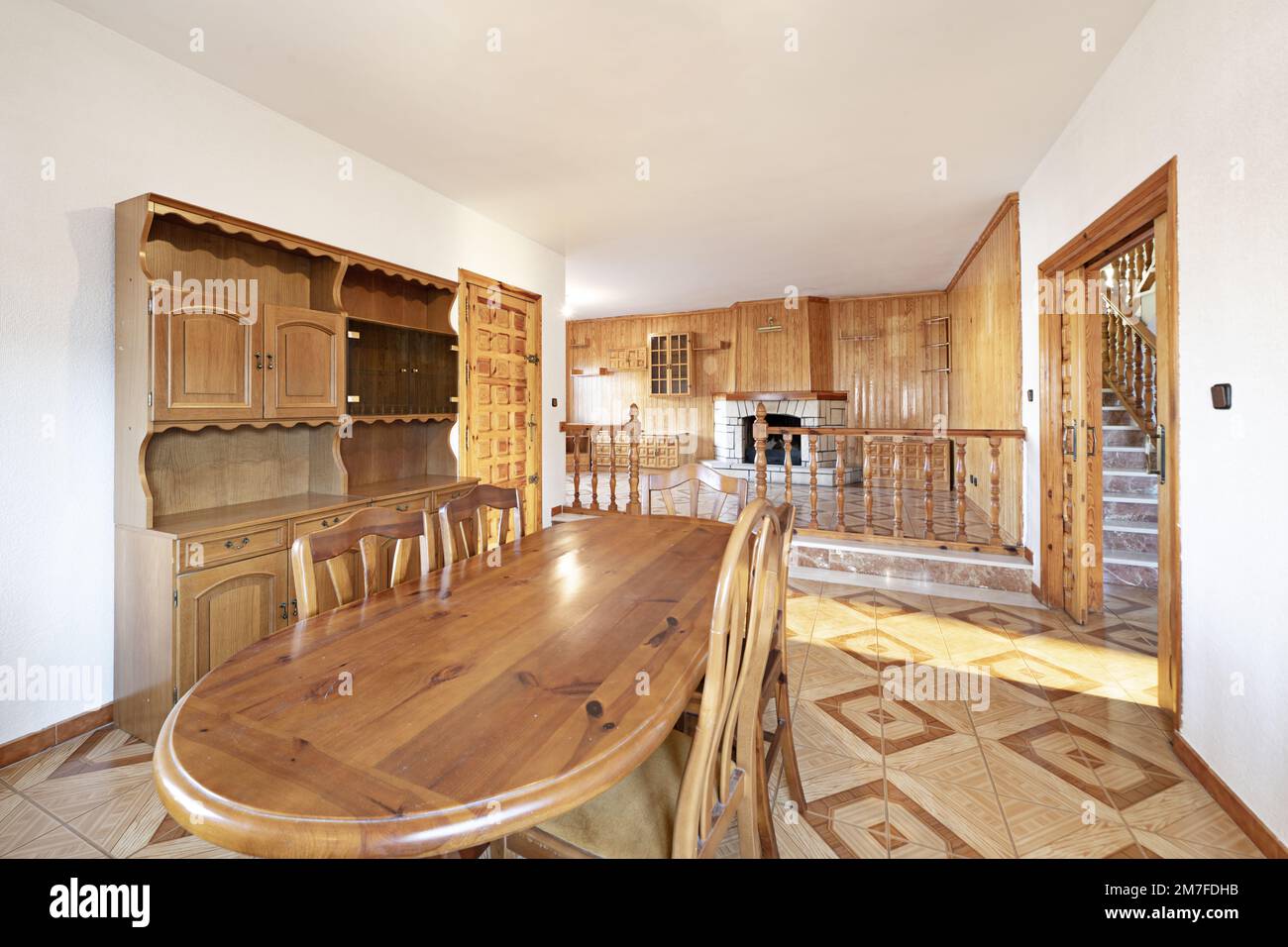 Dining room of a low house with pine wood table, walnut furniture, railing in double height