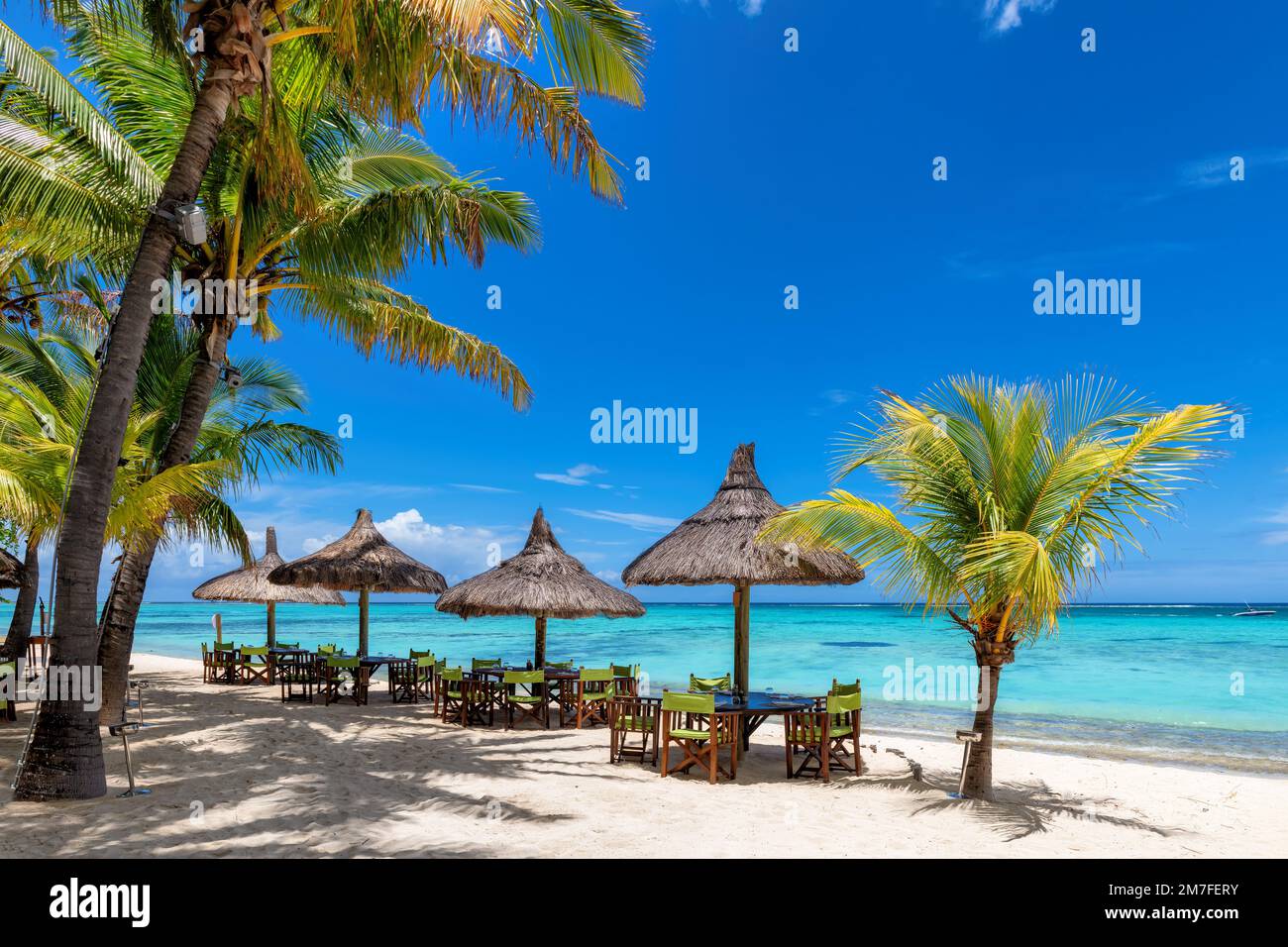 Beach cafe on sandy beach, tables under straw umbrellas, palm trees and beautiful sea on exotic tropical island. Stock Photo