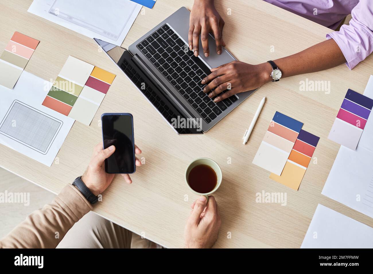 Top view closeup of two designers using laptop while working on UI project in office, flat lay with color swatches Stock Photo