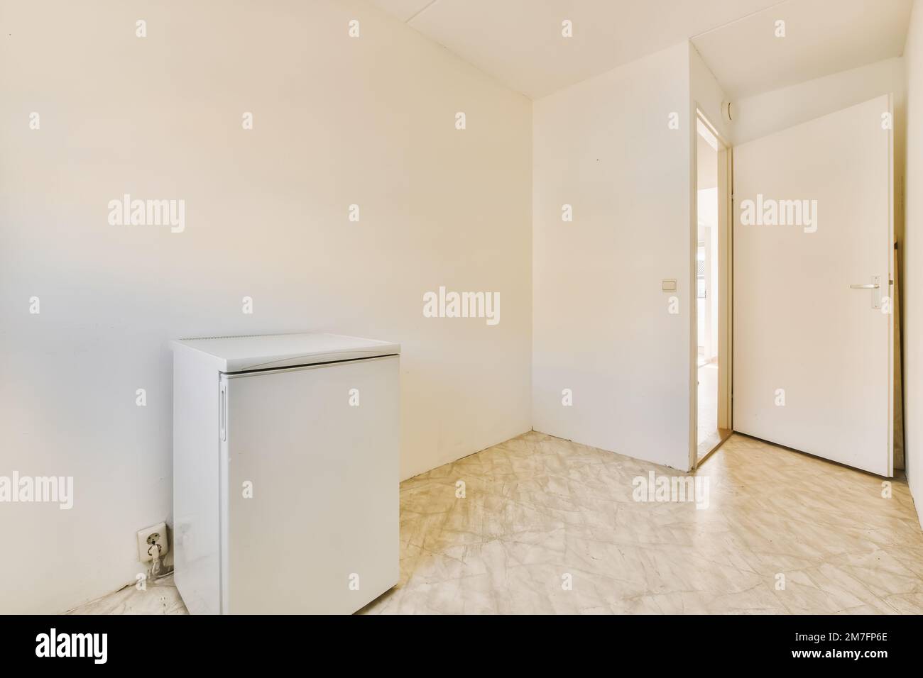 an empty room with a refrigerator freezer in the corner and no one door on the other wall behind it Stock Photo