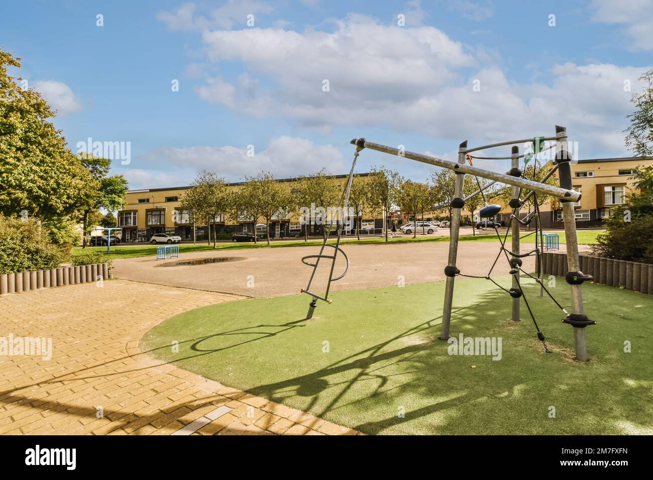 an outdoor playground area with swings, slides and climbing equipment on the ground in front of a school building is in the background Stock Photo