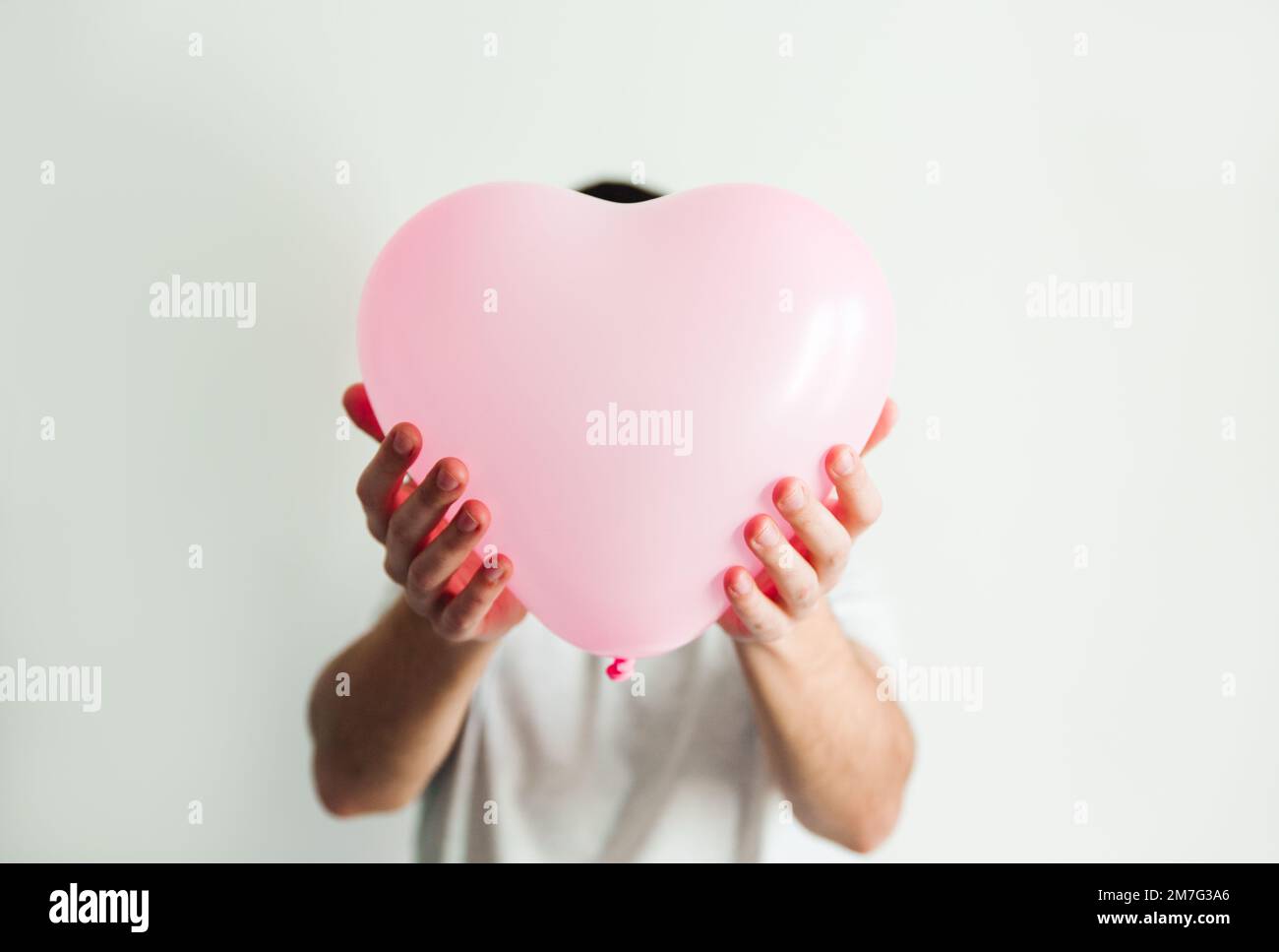 Pink inflatable heart-shaped balloon in hand. White background. Stock Photo