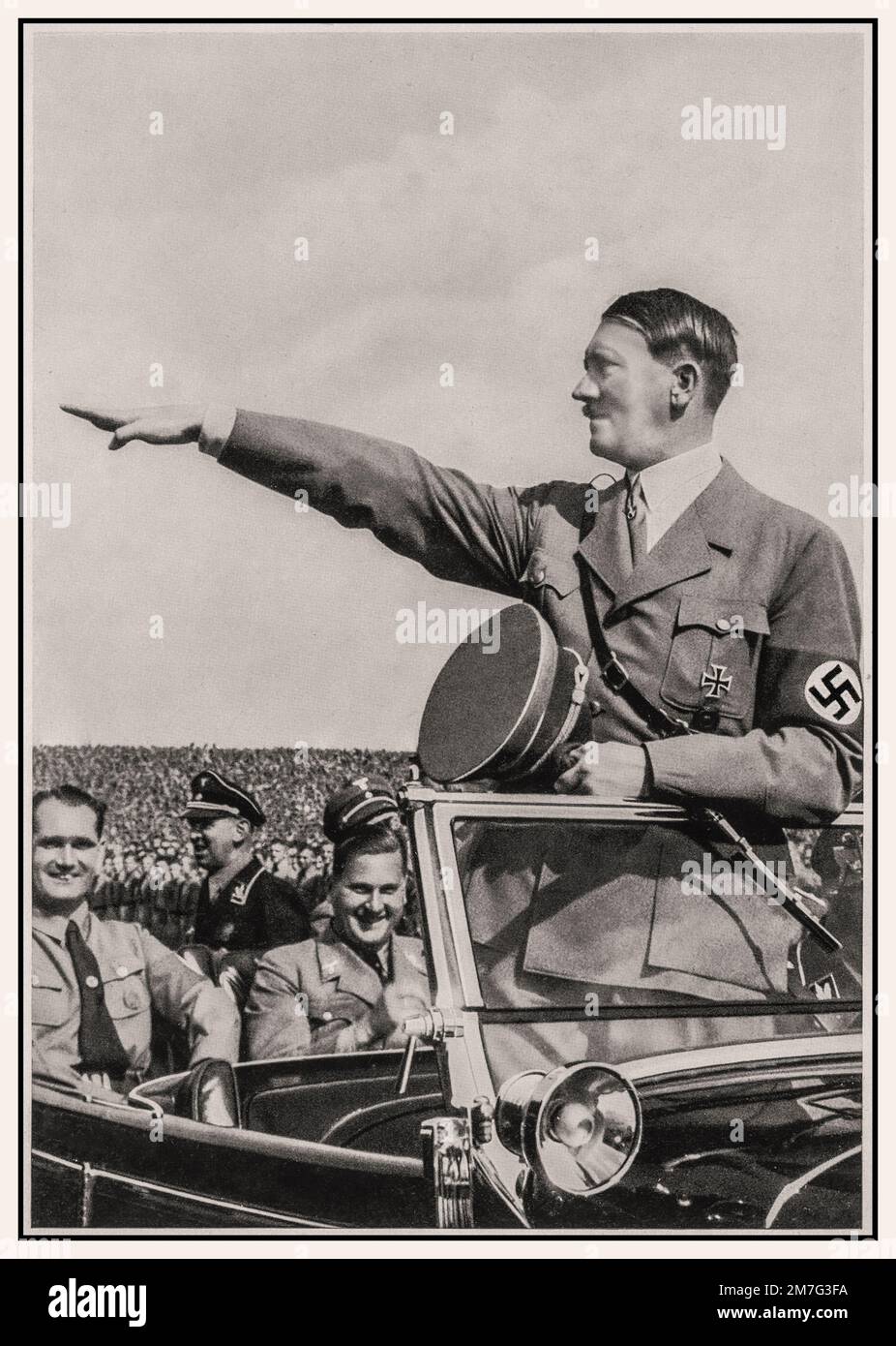 Adolf Hitler wearing a swastika armband at a 1930’s Nazi Party Nuremberg rally, with Rudolf Hess sitting behind, standing in the front of his open top Mercedes motorcar saluting the passing troops of the NSDAP political party military wing Hitler Nuremberg Rally Heil Hitler salute s Nazi Gemany 1930s Stock Photo