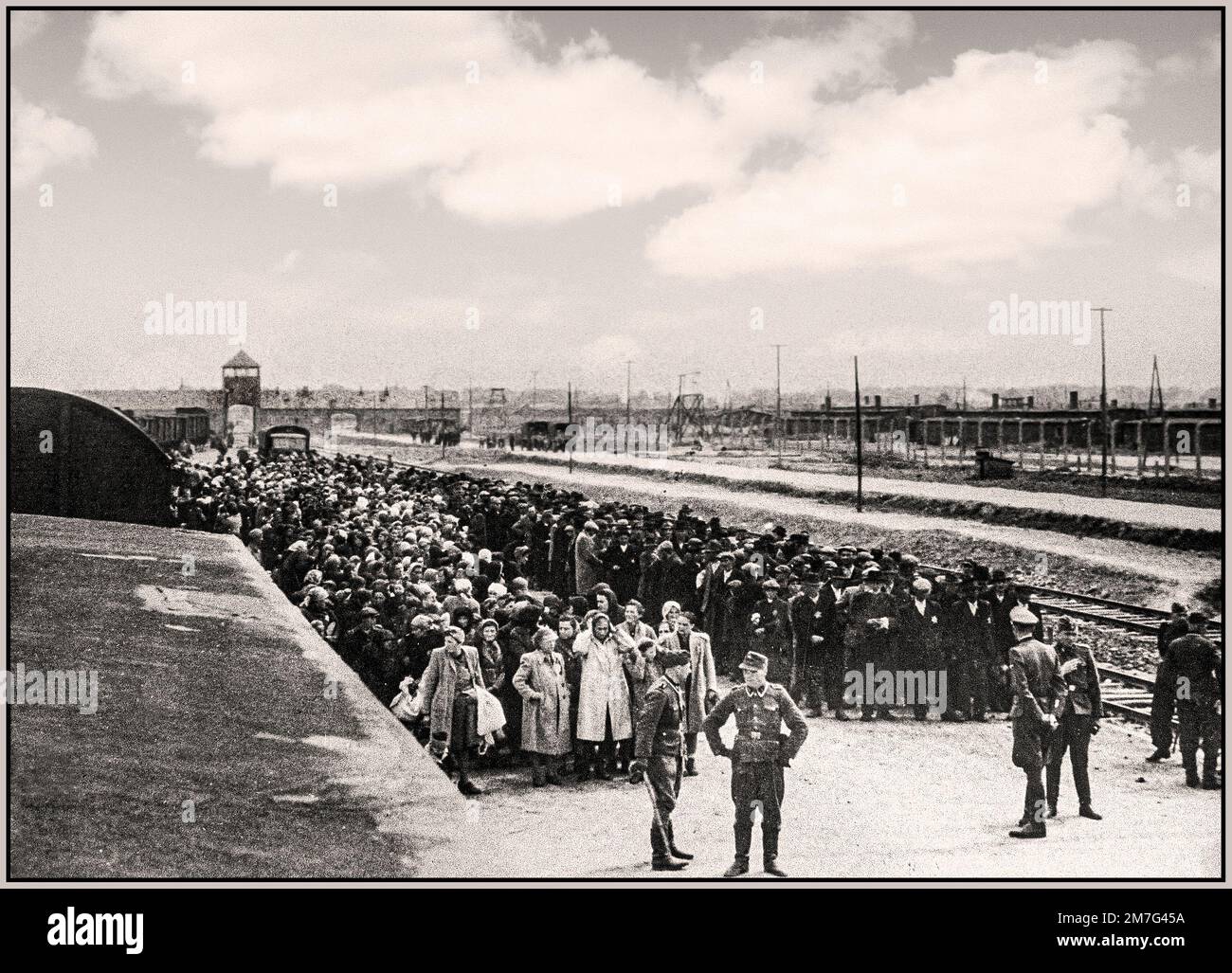 AUSCHWITZ-BIRKENAU HOLOCAUST PRISONERS ARRIVAL- A vision of a hell on earth. 1944, Nazis 'grading' (life or death) unsuspecting prisoners on rail concourse outside entrance to Auschwitz-Birkenau extermination death camp. The infamous Auschwitz camp was started by order of Adolf Hitler in 1940's during the occupation of Poland by Nazi Germany during World War 2, further enabled by Heinrich Luitpold Himmler the Reichsführer of the Schutzstaffel, and leading member of the Nazi Party of Germany Stock Photo