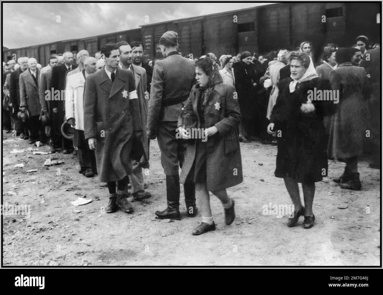 AUSCHWITZ-BIRKENAU HOLOCAUST PRISONERS ARRIVAL WEARING YELLOW STARS OF DAVID - A vision of hell on earth. 1944, Nazis 'grading' (life or death) unsuspecting prisoners on rail concourse outside entrance to Auschwitz-Birkenau extermination death camp. The infamous Auschwitz camp was started by order of Adolf Hitler in 1940's during the occupation of Poland by Nazi Germany during World War 2, further enabled by Heinrich Luitpold Himmler the Reichsführer of the Schutzstaffel, and leading member of the Nazi Party of Germany Stock Photo
