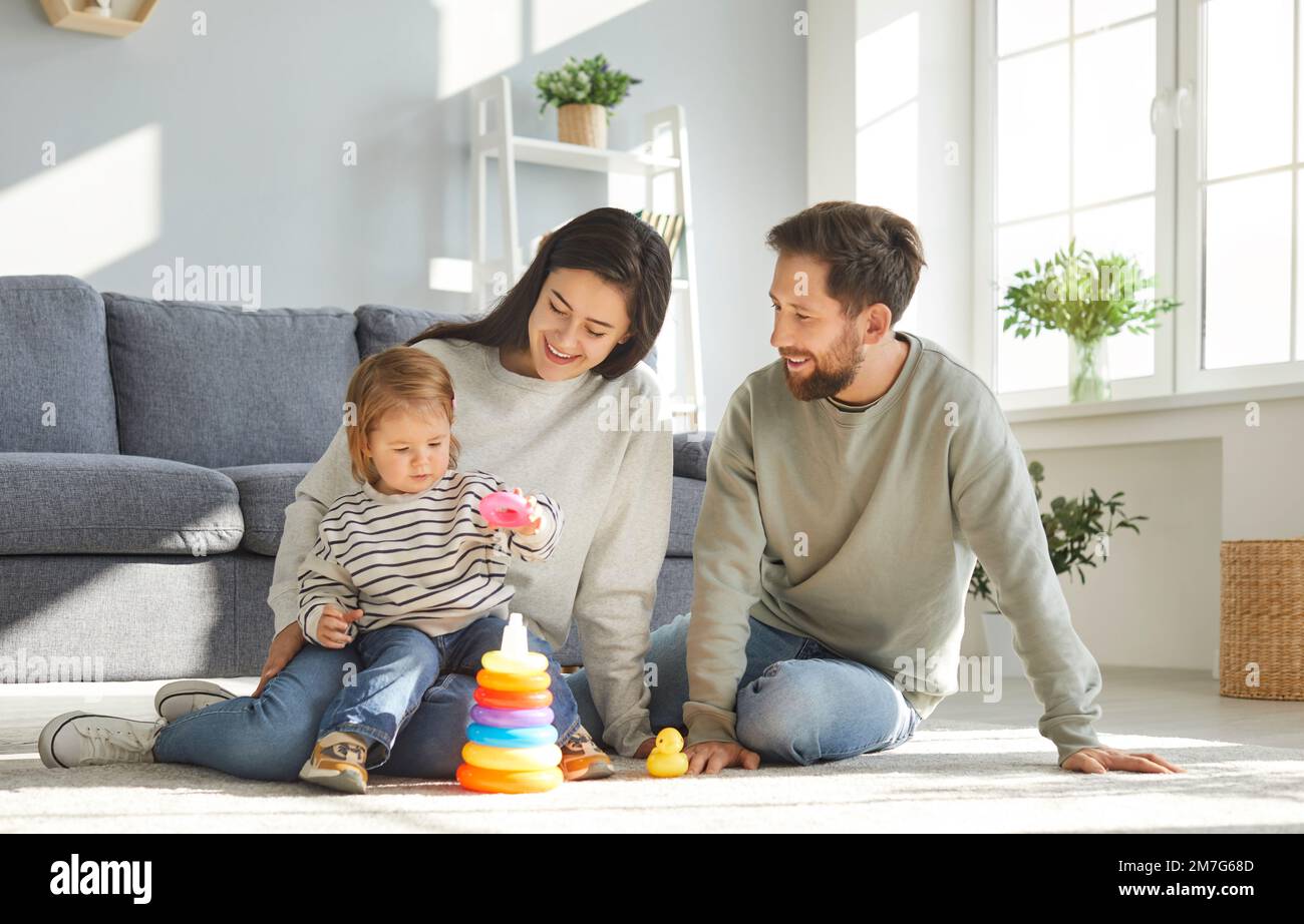Family with their little daughter builds rainbow tower while playing on floor of children's room. Stock Photo