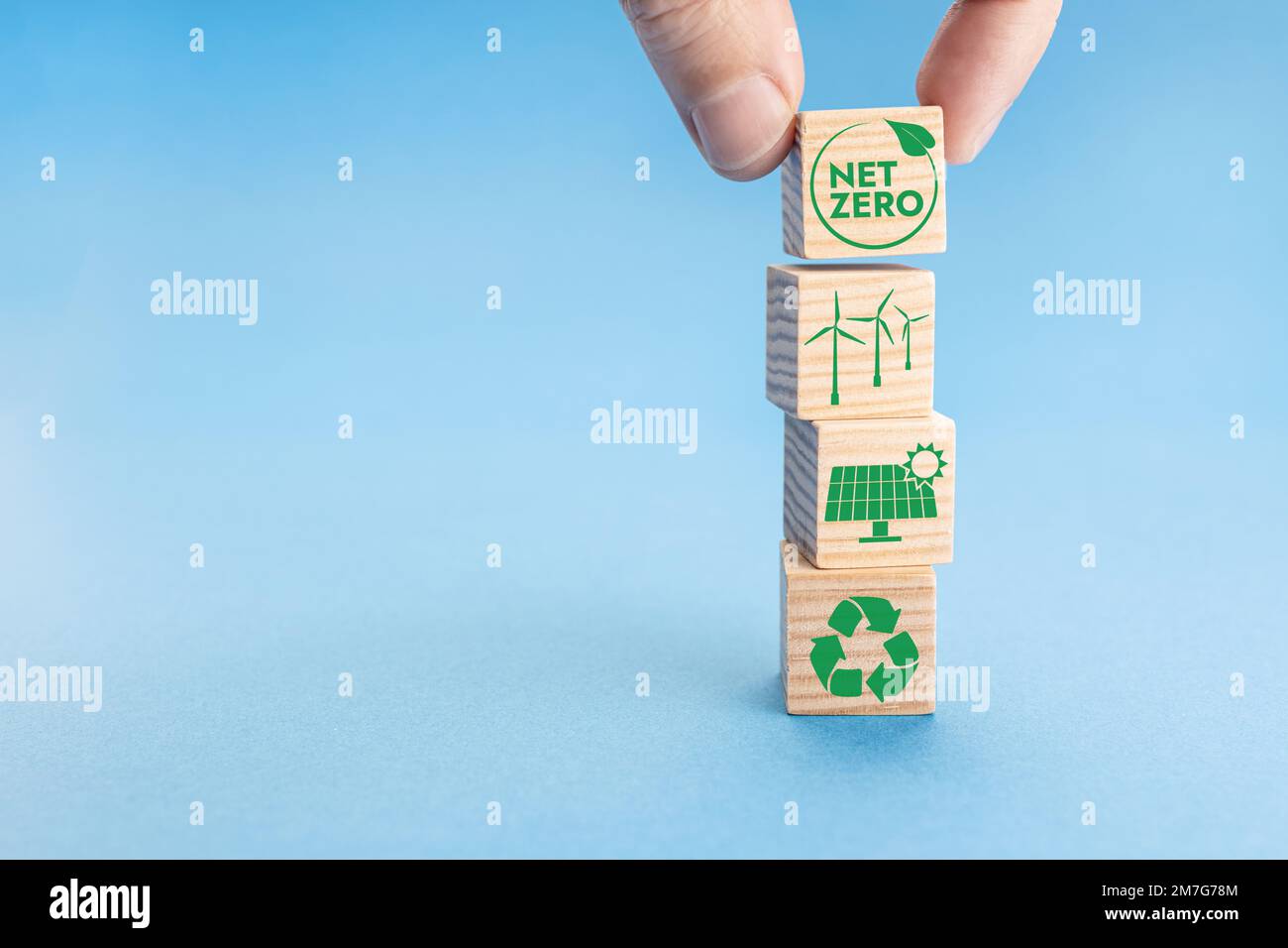 Net Zero and Carbon Neutral Concept. Hand putting wood block with Net Zero icon on top of others with green energy icons. Blue background. Copy space Stock Photo