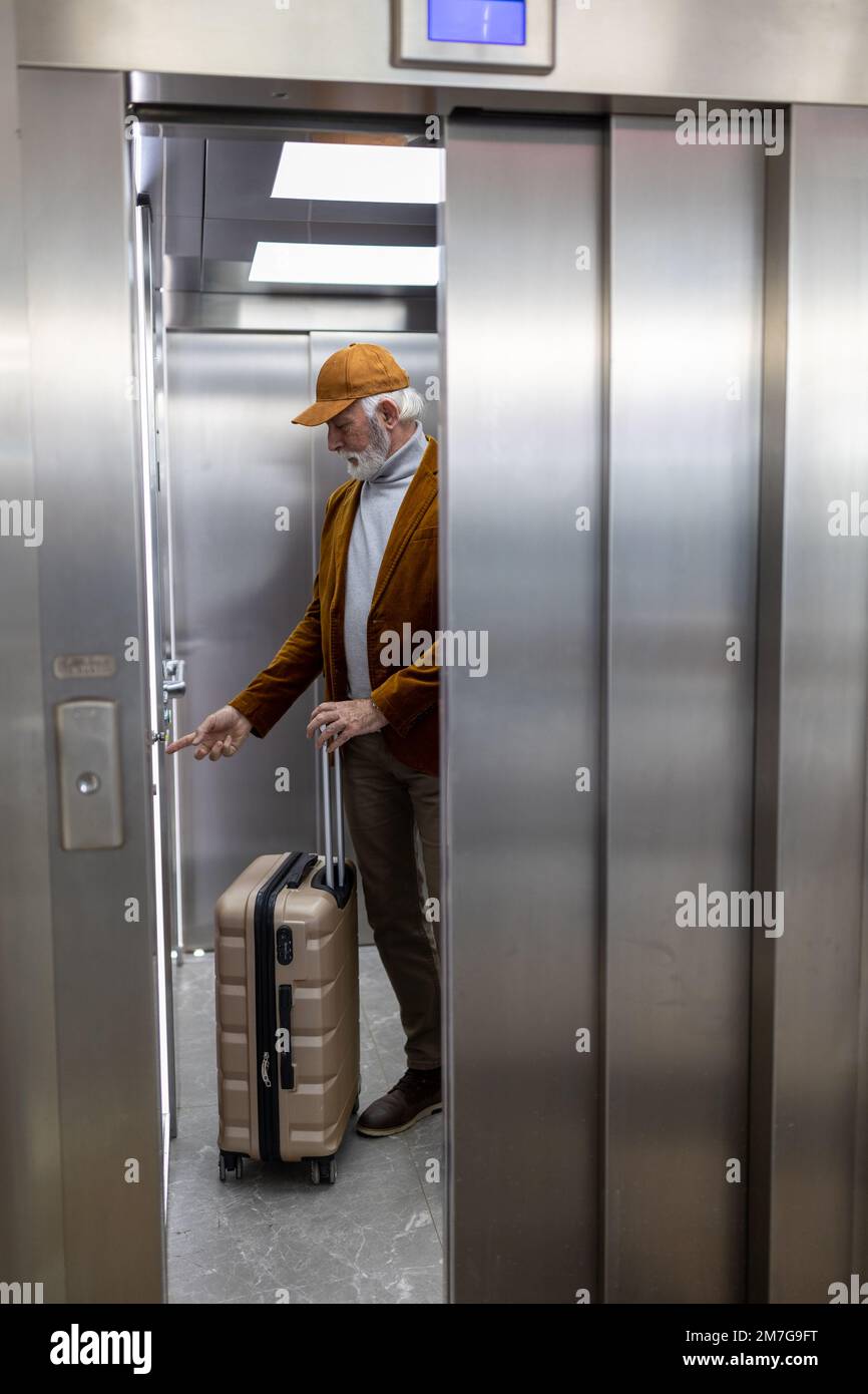 Senior man with suitcase touching button in elevator on train station Stock Photo