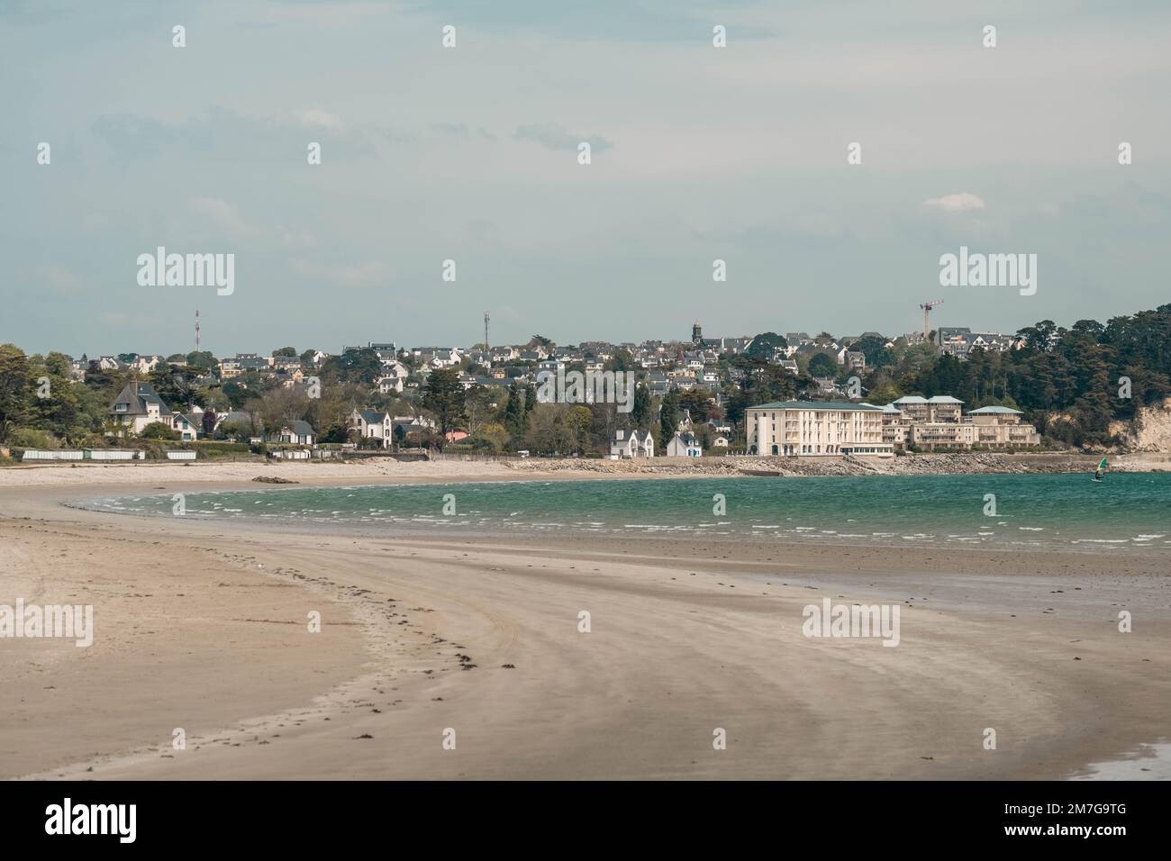 A serene beach scene in Brittany, France, with a cloudy sky and houses in the background. Stock Photo