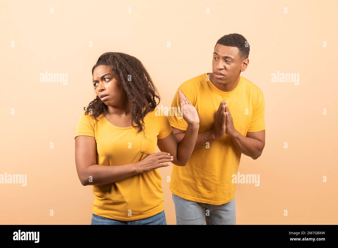 Black husband trying to talk and reconcile with offended wife, standing over yellow studio background Stock Photo