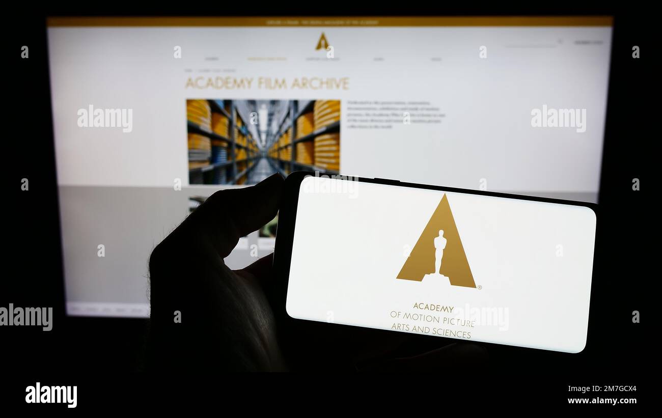 Person holding cellphone with logo of Academy of Motion Picture Arts and Sciences (AMPAS) on screen in front of web page. Focus on phone display. Stock Photo