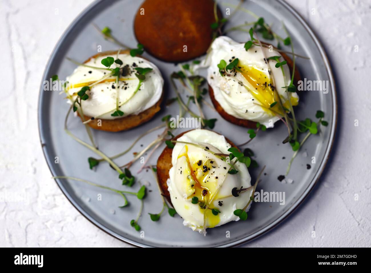 Poached eggs with microgreens on a crispy bun on a plate. Stock Photo