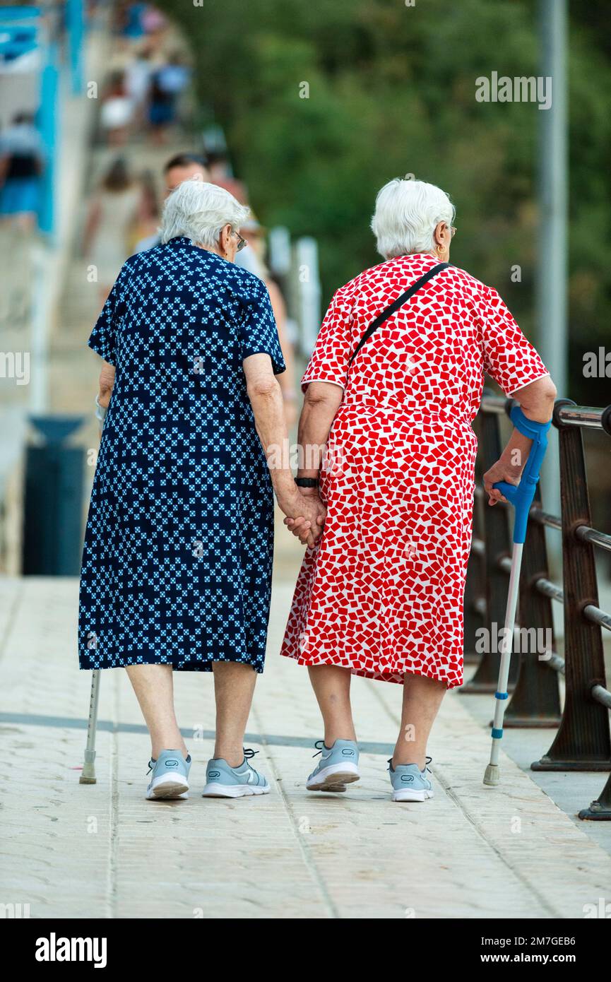 Two elderly ladies walk hand in hand on the waterfront promenade of Porto Cristo, Mallorca. Stock Photo