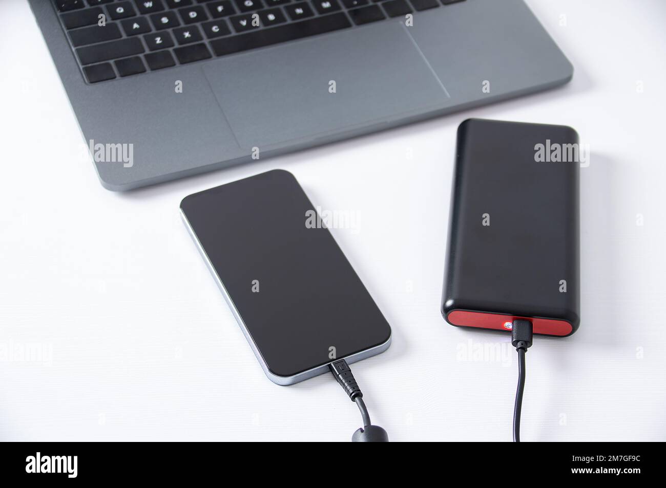 USB charger plugged in to smart phone with power bank, mobile phone battery on desk at office. Stock Photo