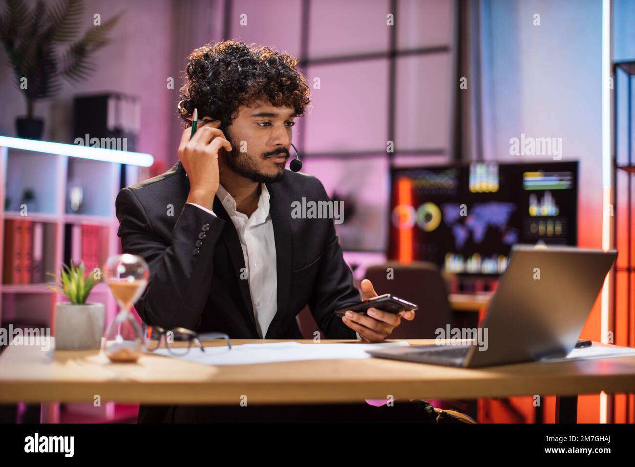 Deadline concept of project, working at evening time in office. Serious businessman, broker, financial expert in suit and headset working using laptop computer. Stock Photo
