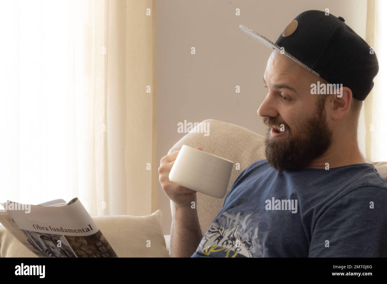 Caucasian bearded man drinking coffee Reading a magazine. "Obra fundamental" means fundamental work. Stock Photo